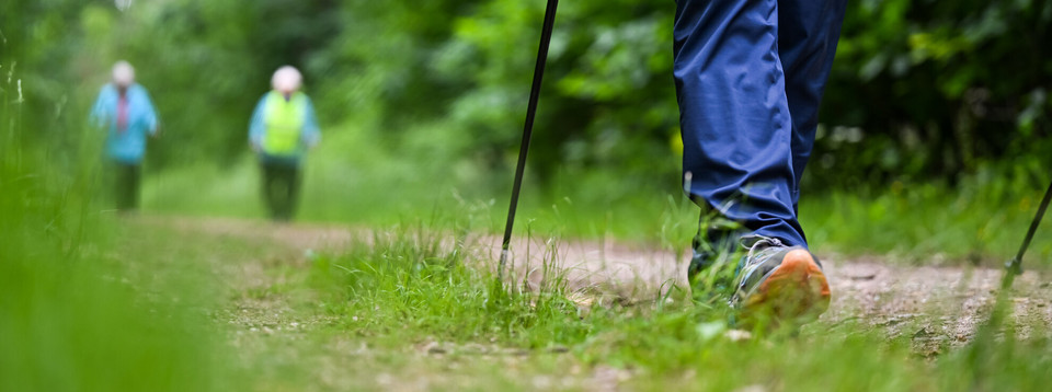 Person mit Walkingstöcken angedeutet, Hintergrund verschwommen