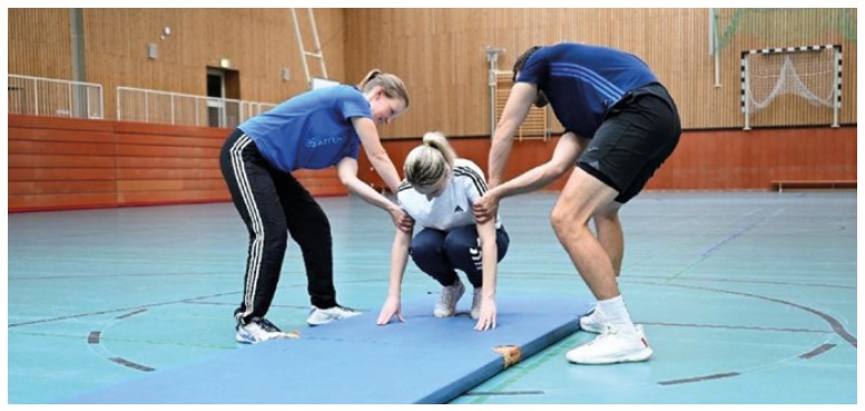 Der Drehgriff vorwärts zum Beispiel bei einer Rolle vorwärts, je nach Entwicklungsstand der Teilnehmer*innen wird entschieden, ob zwei Personen oder eine Person helfen.