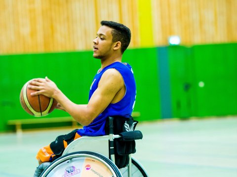 Rollstuhlfahrer beim Basketballspielen in Sporthalle.