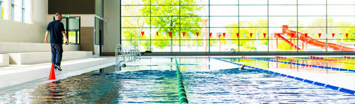 Person zieht Bahnen im Schwimmbad, Trainer läuft am Rand mit