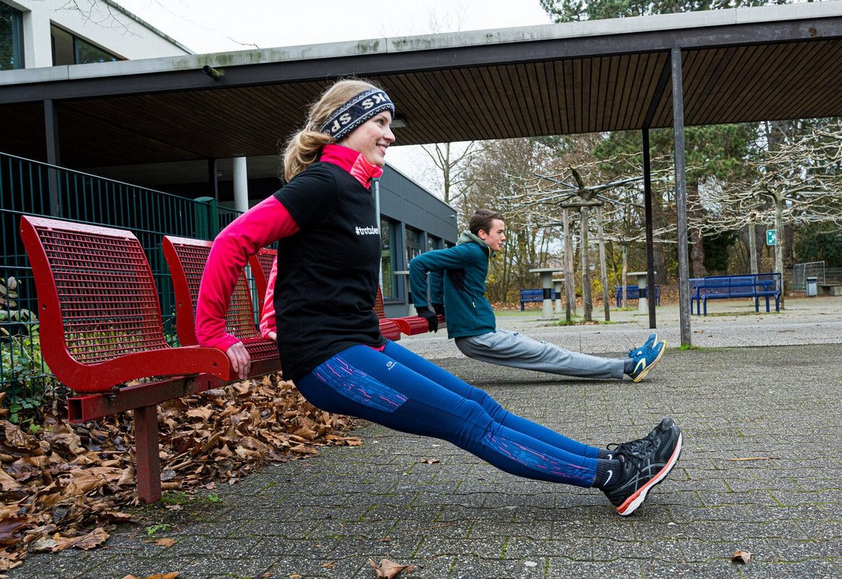 Zwei Menschen machen draußen Übungen an einer Bank