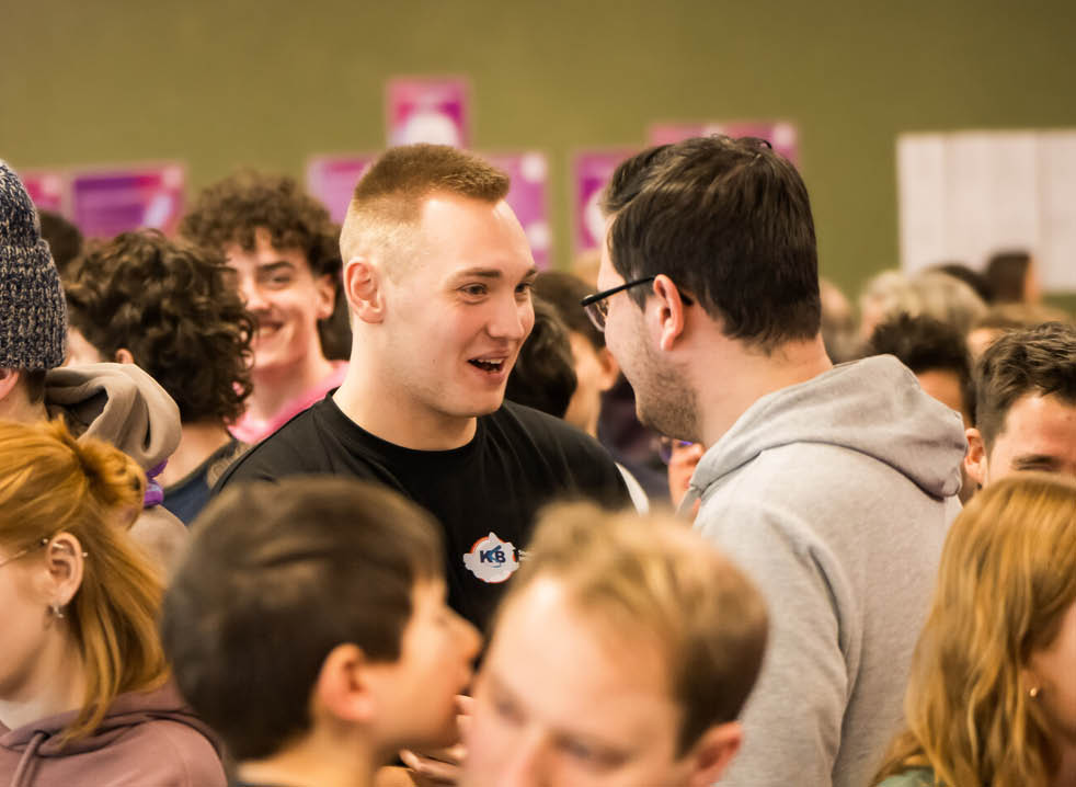 Zwei Sporthelfer im Gespr ch bei einem Netzwerktreffen inmitten vieler Sporthelfer